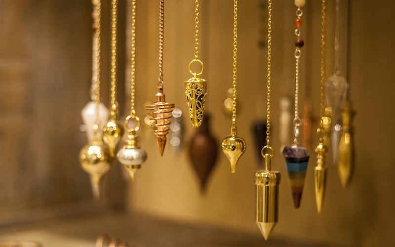 colección de péndulos suspendidos en exhibición. Penden de cadenas. Parece piezas de joyería. La mayoría son de color dorado.